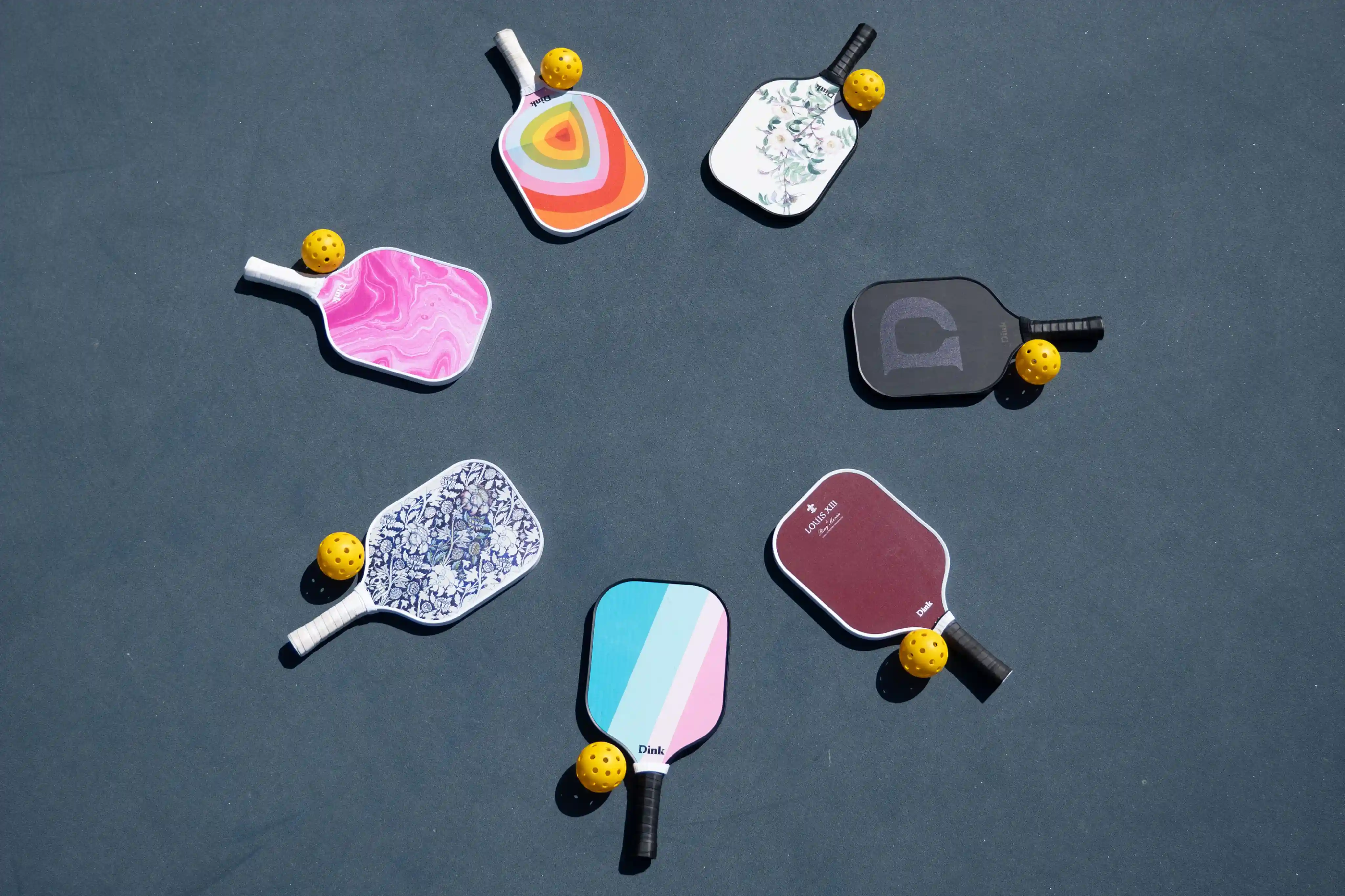 A variety of colorful pickleball paddles and yellow pickleballs displayed on a blue court.